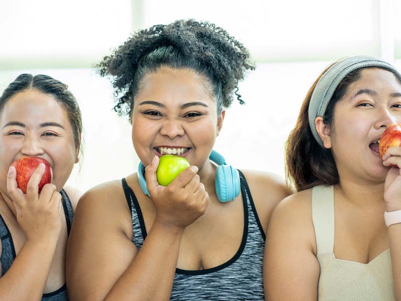 Drei Übergewichtige beissen in einen Apfel